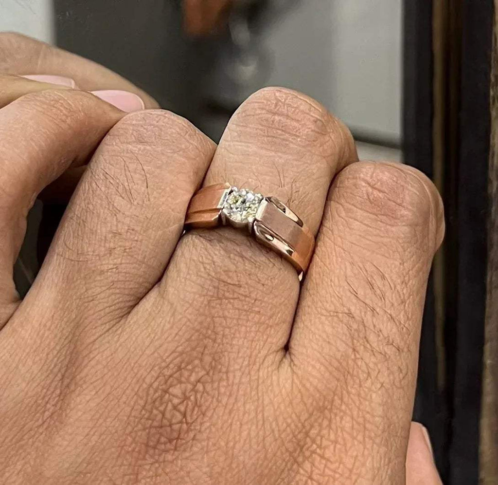 A man's hand holding a diamond solitaire ring with a gold band.