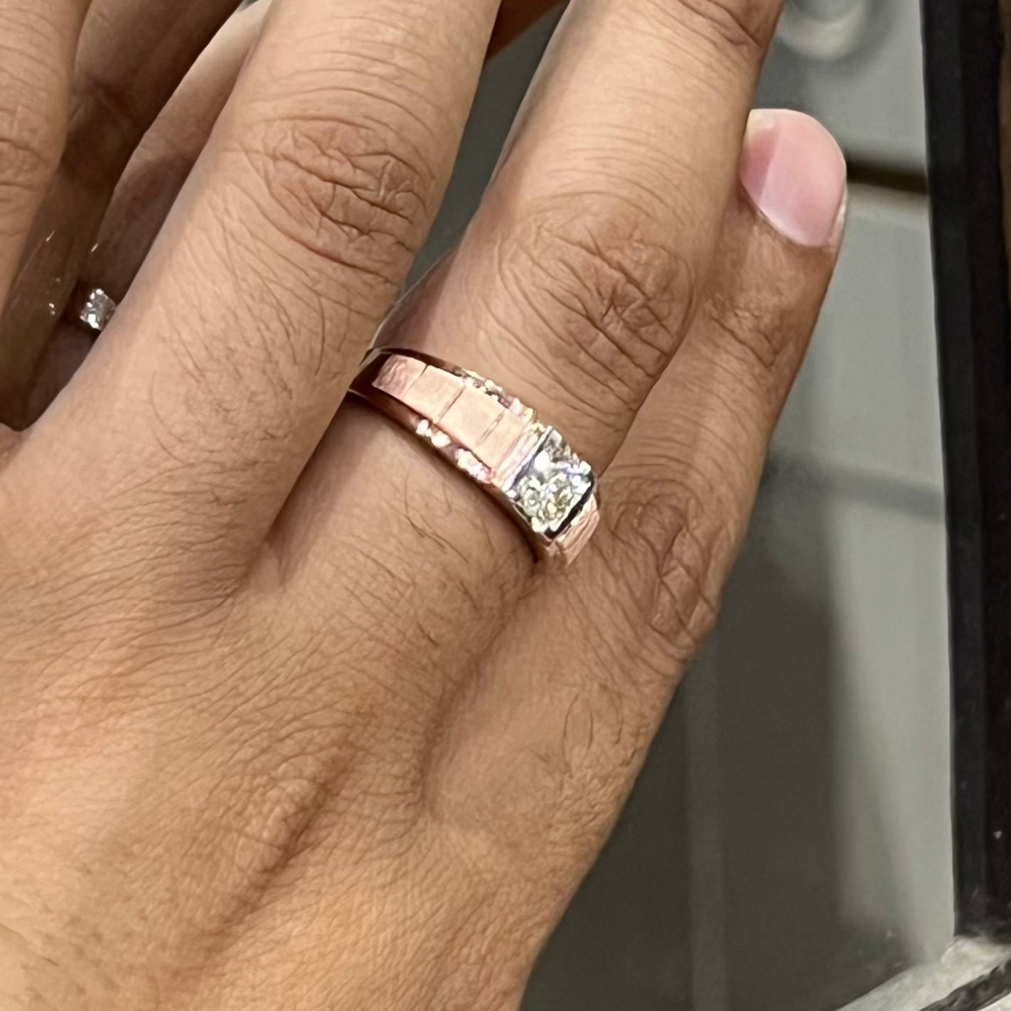 A man's hand displaying a gold band with a central genuine diamond solitaire ring.