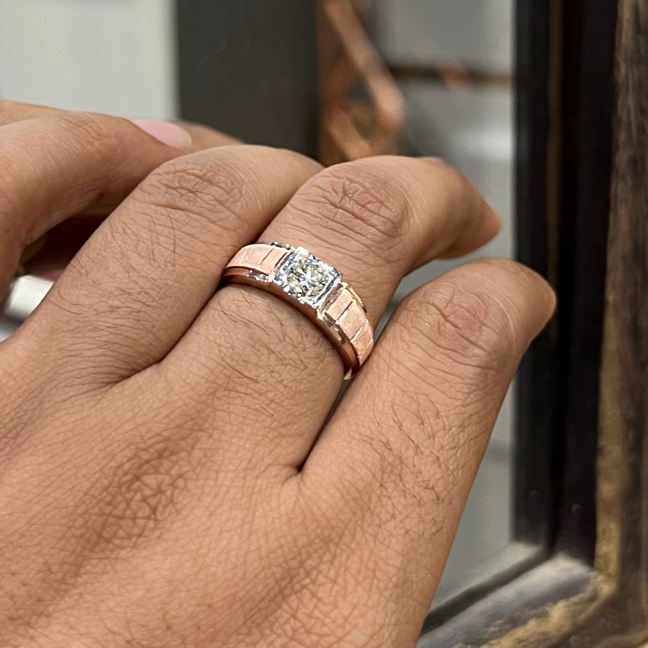 A man's hand displaying a gold band with a central genuine diamond solitaire ring.