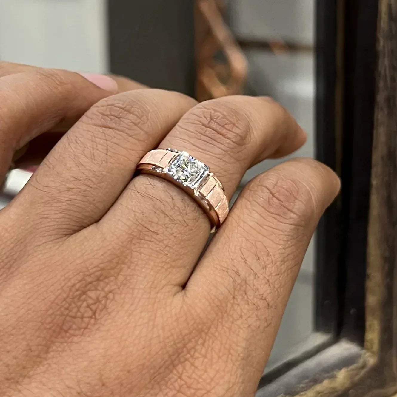 A man's hand displaying a gold band with a central genuine diamond solitaire ring.