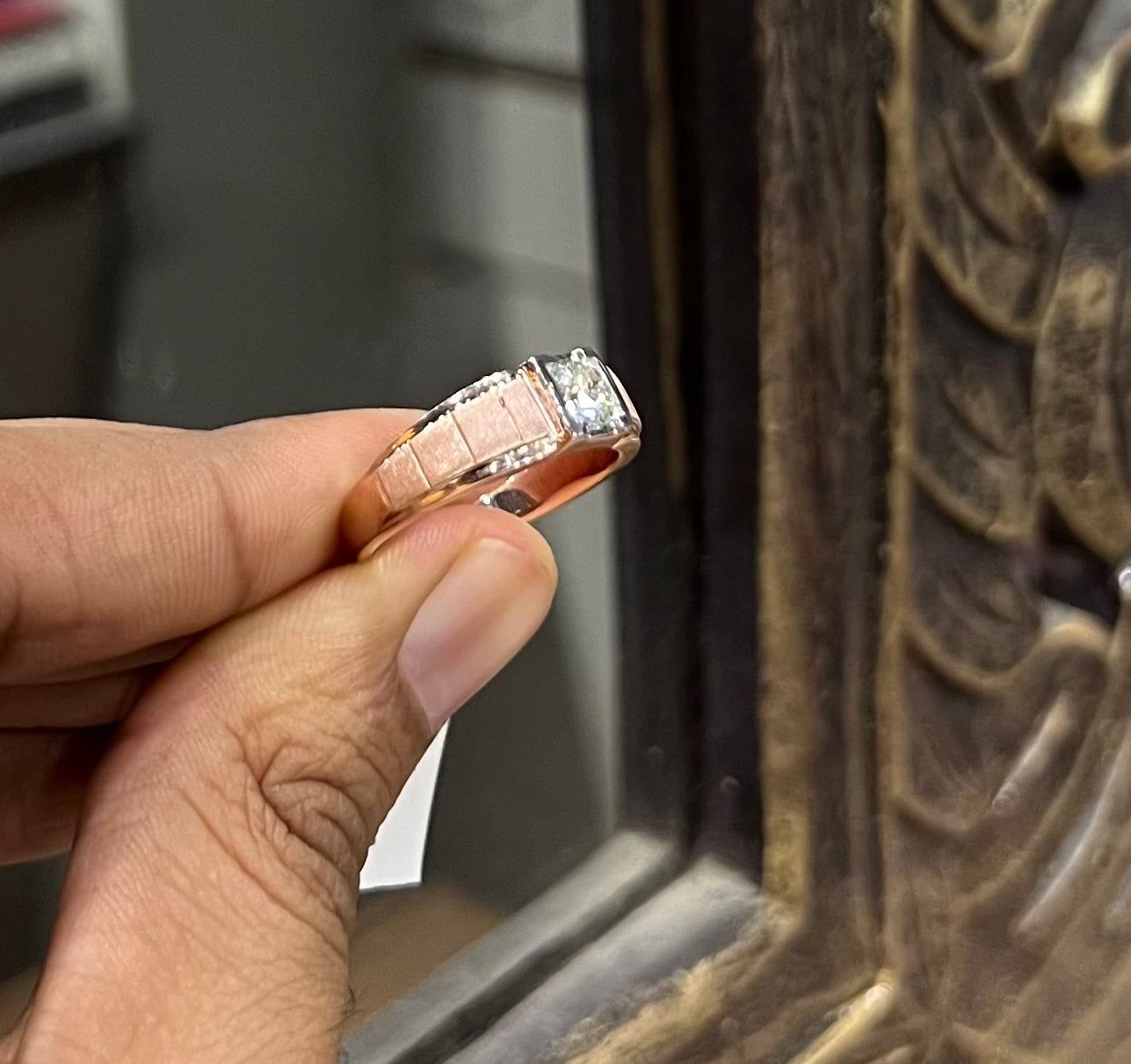 A man's hand displaying a gold band with a central genuine diamond solitaire ring.