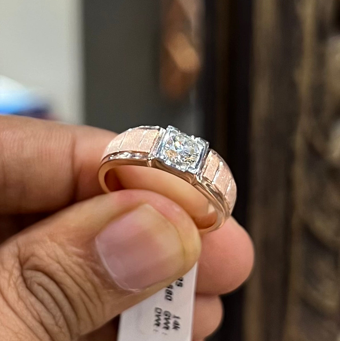 A man's hand displaying a gold band with a central genuine diamond solitaire ring.