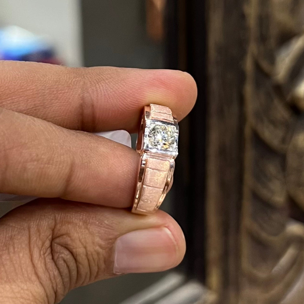 A man's hand displaying a gold band with a central genuine diamond solitaire ring.