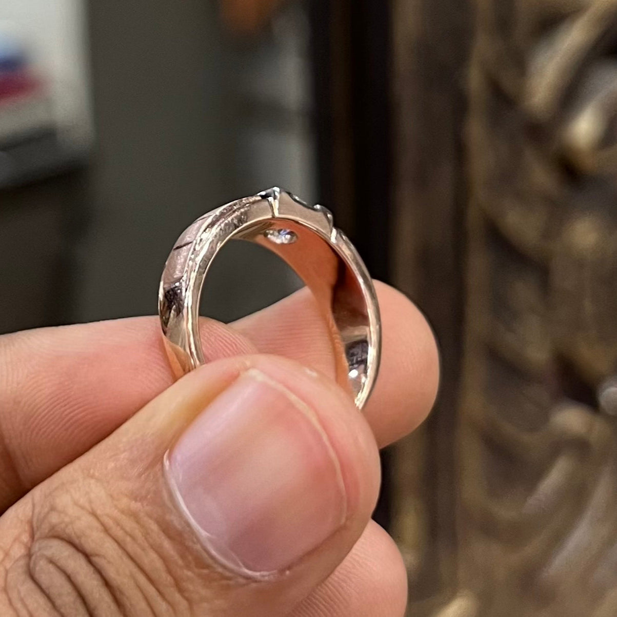 A man's hand displaying a gold band with a central genuine diamond solitaire ring.