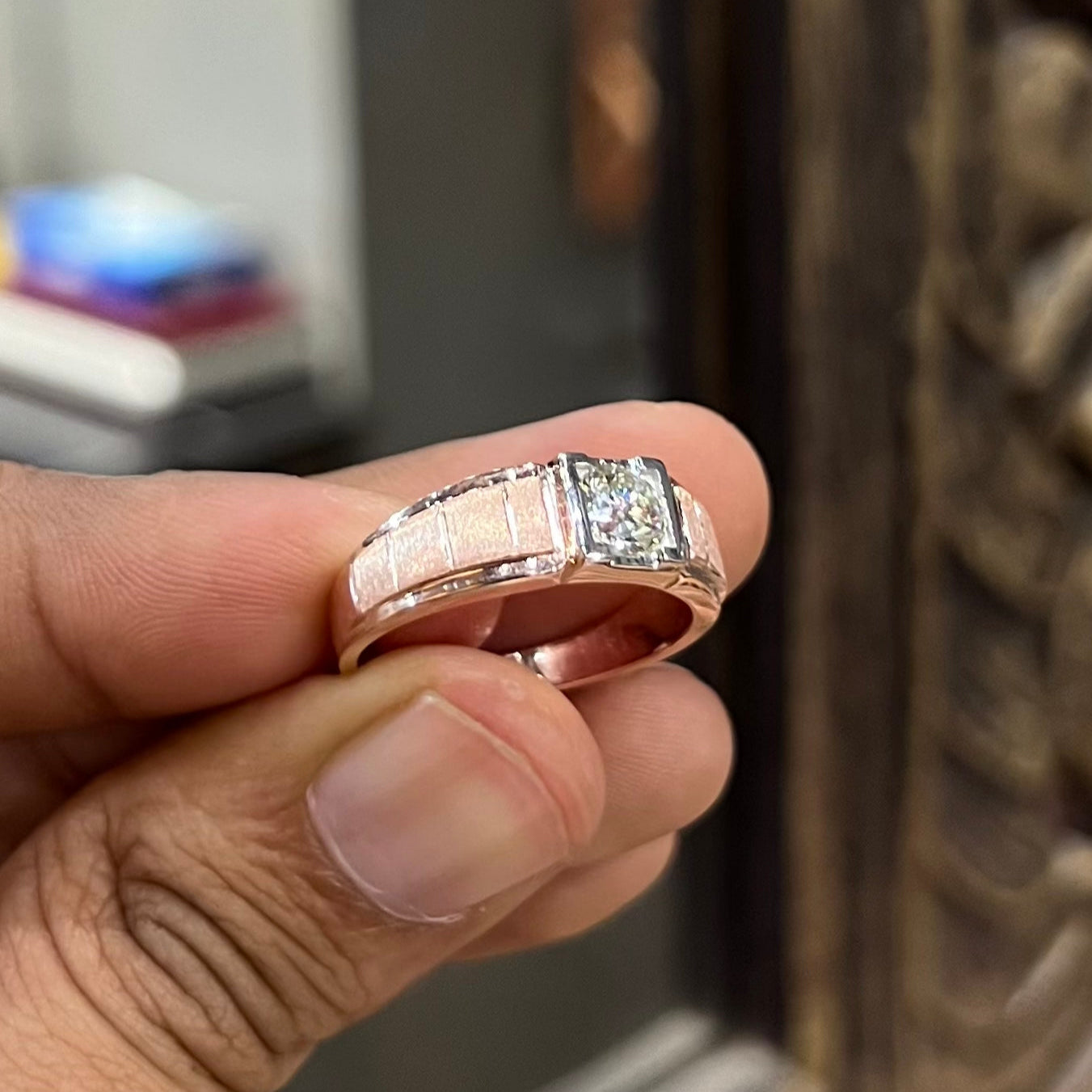 A man's hand displaying a gold band with a central genuine diamond solitaire ring.