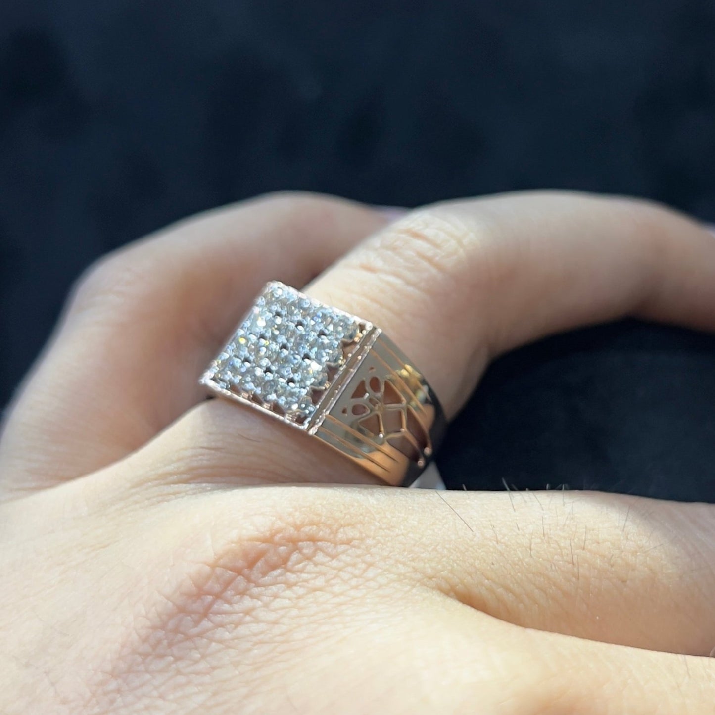 A man's hand displaying a gold band ring with smaller round cut diamonds.