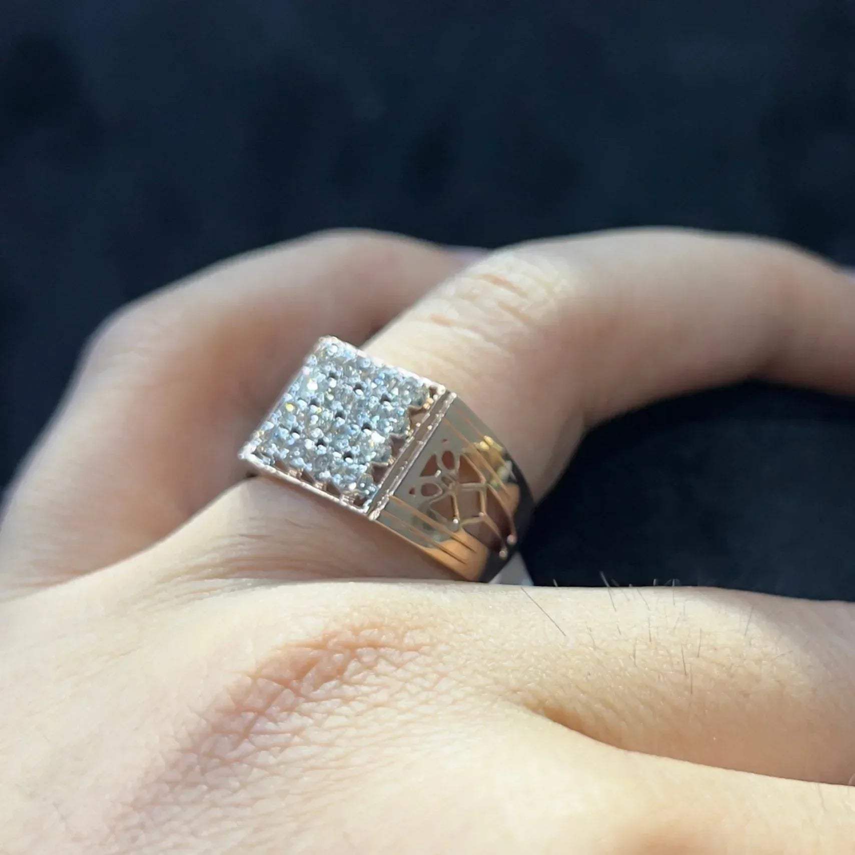 A man's hand displaying a gold band ring with smaller round cut diamonds.