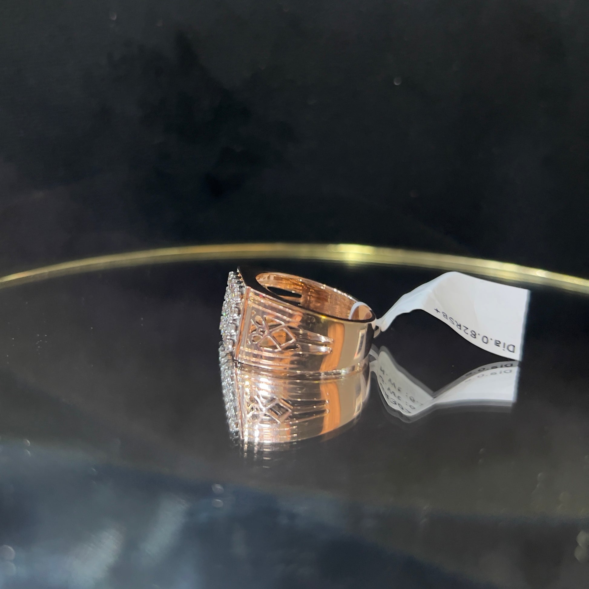 A gold band ring with smaller round cut diamonds is displaying on a reflective surface.