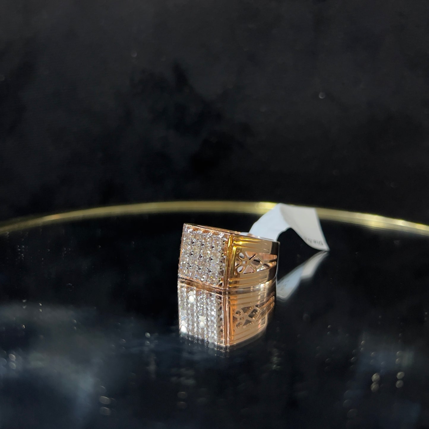 A gold band ring with smaller round cut diamonds is displaying on a reflective surface.