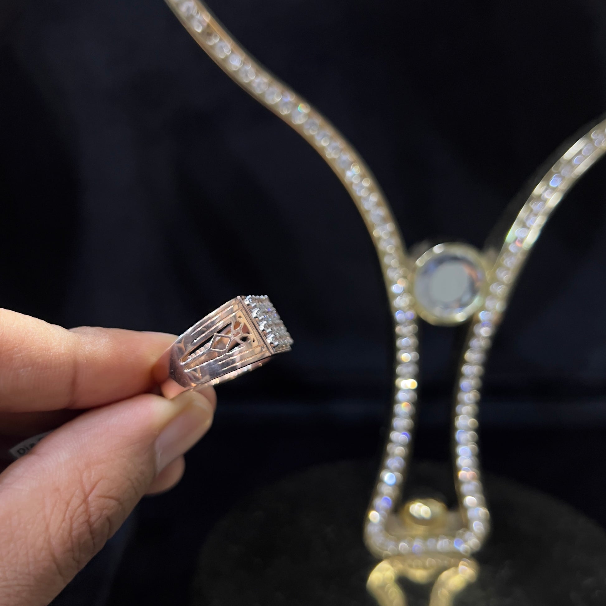 A man's hand displaying a gold band ring with smaller round cut diamonds.