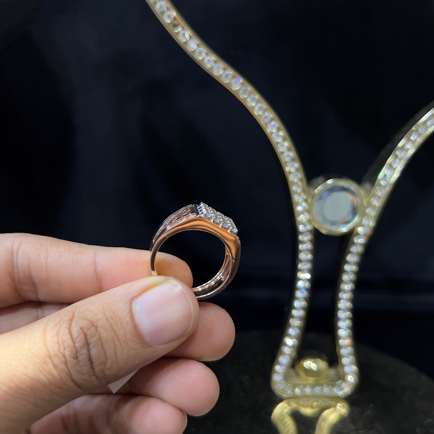 A man's hand displaying a gold band ring with smaller round cut diamonds.