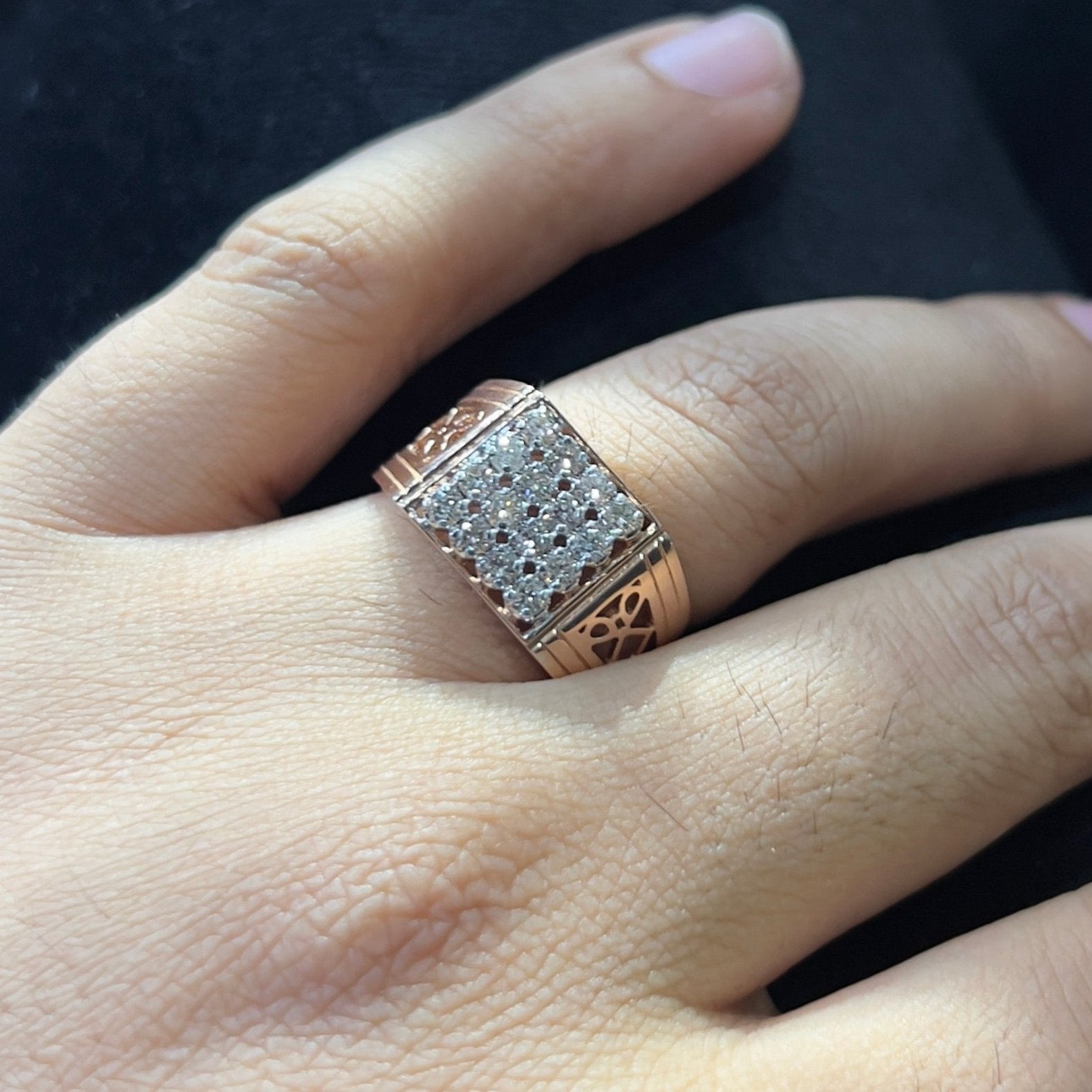 A man's hand displaying a gold band ring with smaller round cut diamonds.