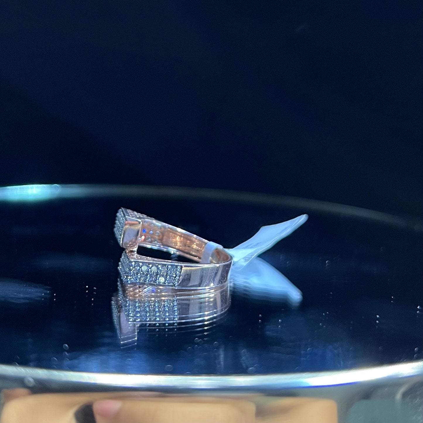 A reflective surface displaying a 14K gold diamond ring with a solid band and a small diamond inlay on the top surface.