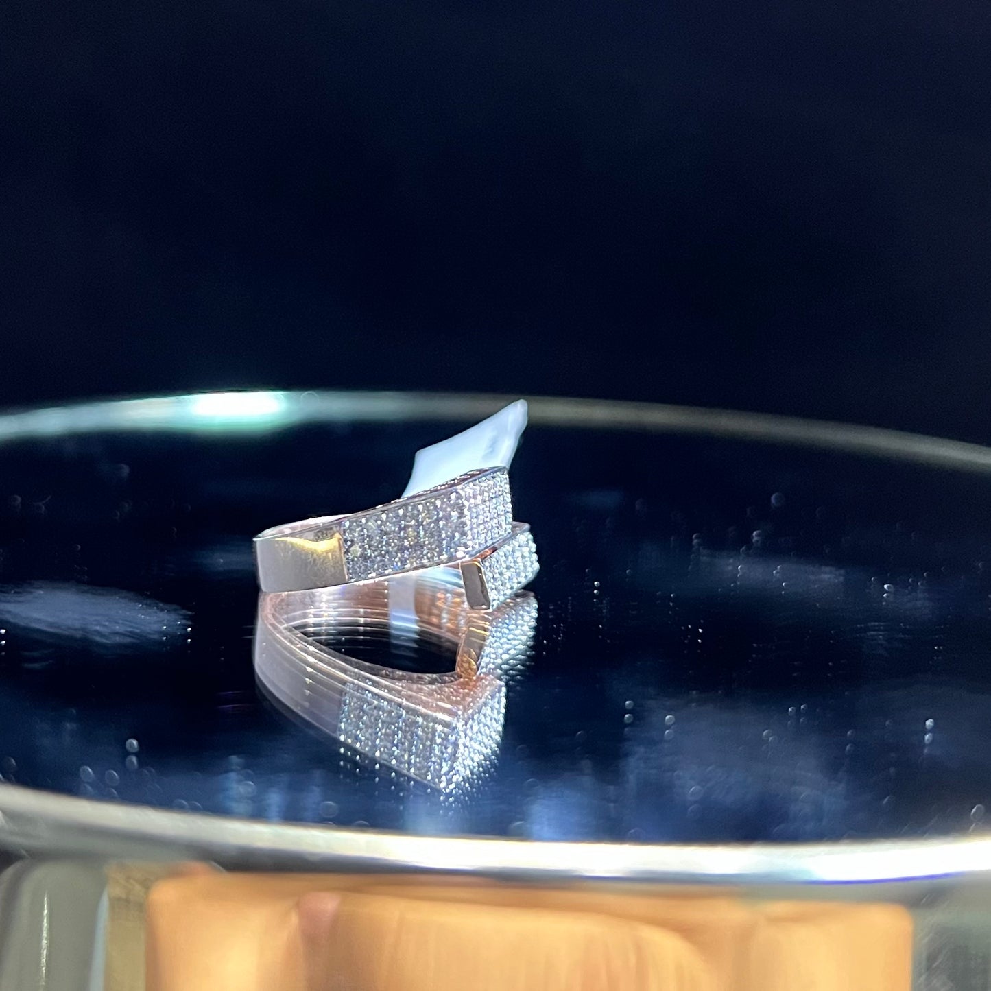 A reflective surface displaying a 14K gold diamond ring with a solid band and a small diamond inlay on the top surface.