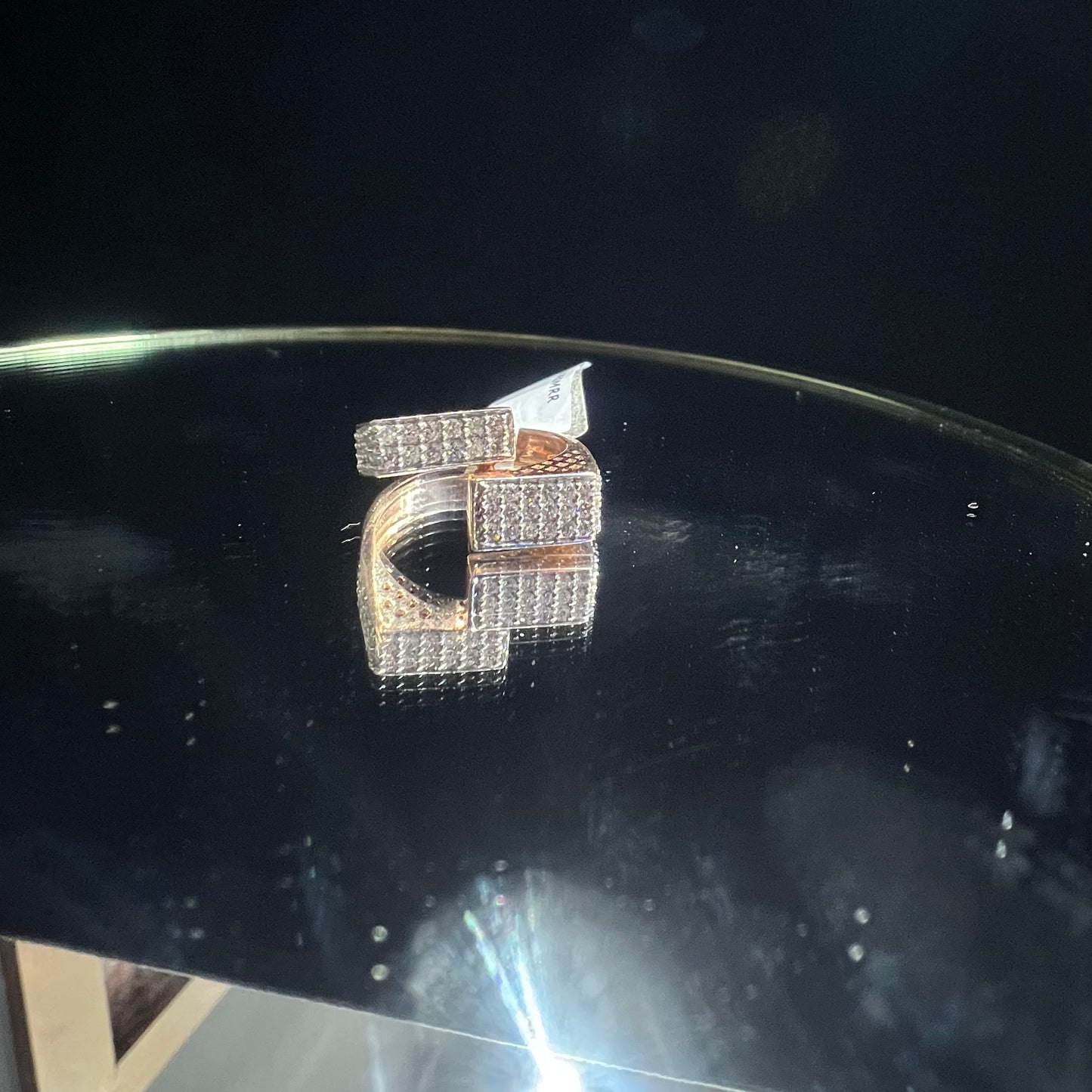 A reflective surface displaying a 14K gold diamond ring with a solid band and a small diamond inlay on the top surface.