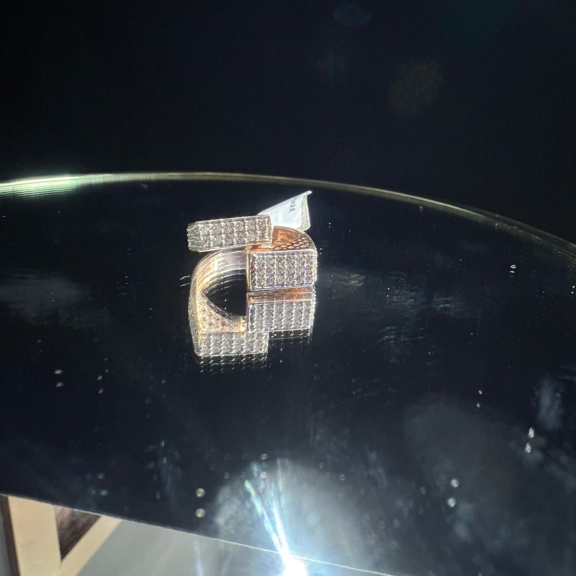 A reflective surface displaying a 14K gold diamond ring with a solid band and a small diamond inlay on the top surface.