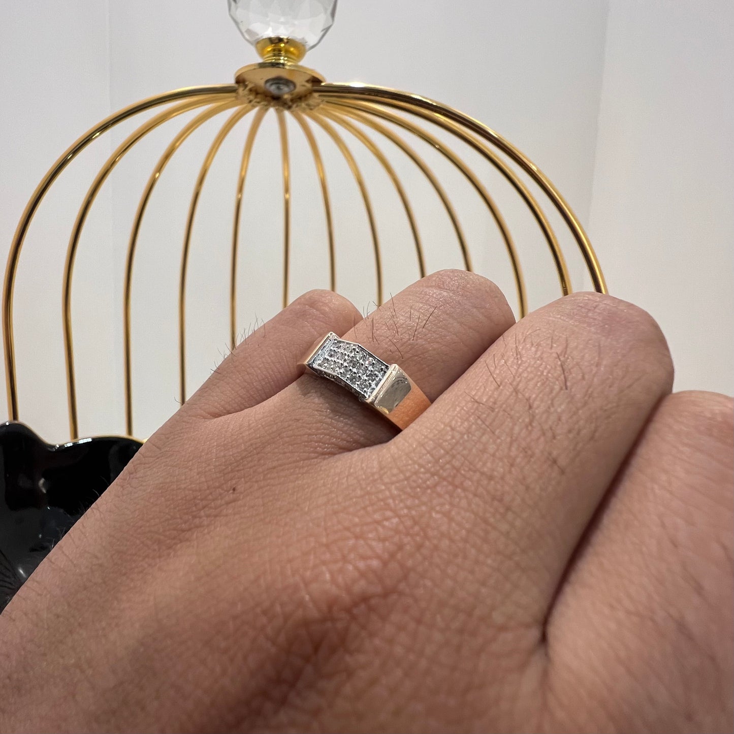 A man's hand holding a gold-banded ring with a large, clear crystal on top, and a smaller, real diamond on the band.
