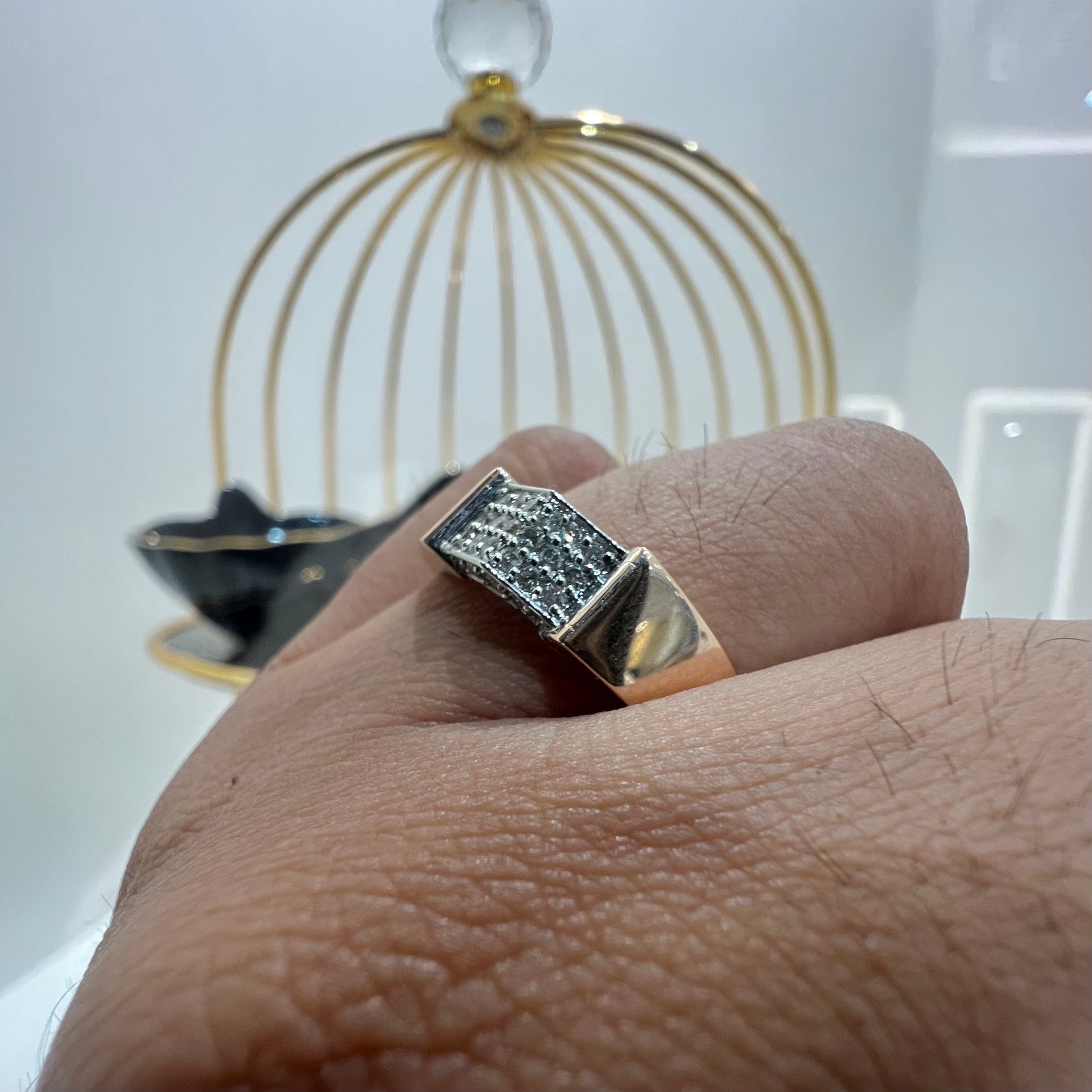 A man's hand holding a gold-banded ring with a large, clear crystal on top, and a smaller, real diamond on the band.