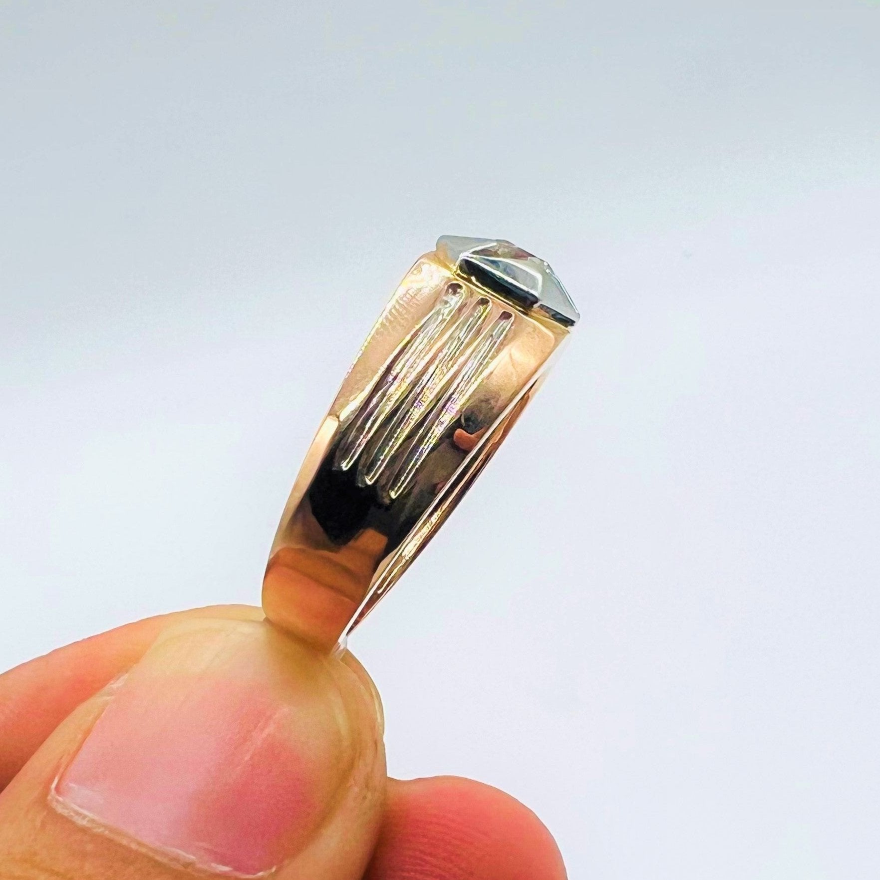 A man's hand displaying a gold solitaire diamond ring hold by his two fingers from the vertical side.