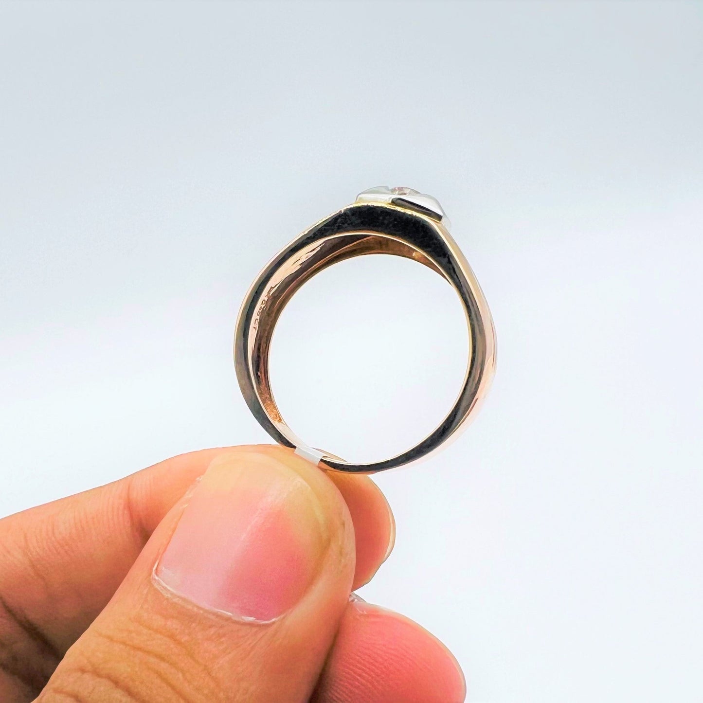 A man's hand displaying a gold solitaire diamond ring hold by his two fingers from the side.
