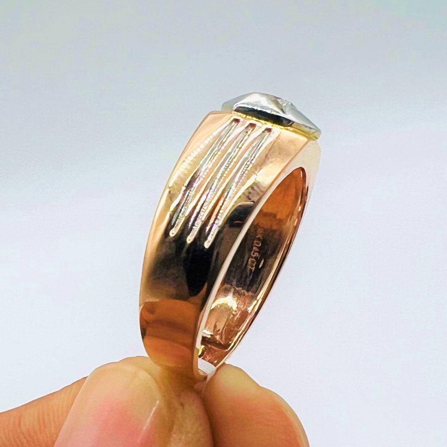 A man's hand displaying a gold solitaire diamond ring hold by his two fingers from the side.