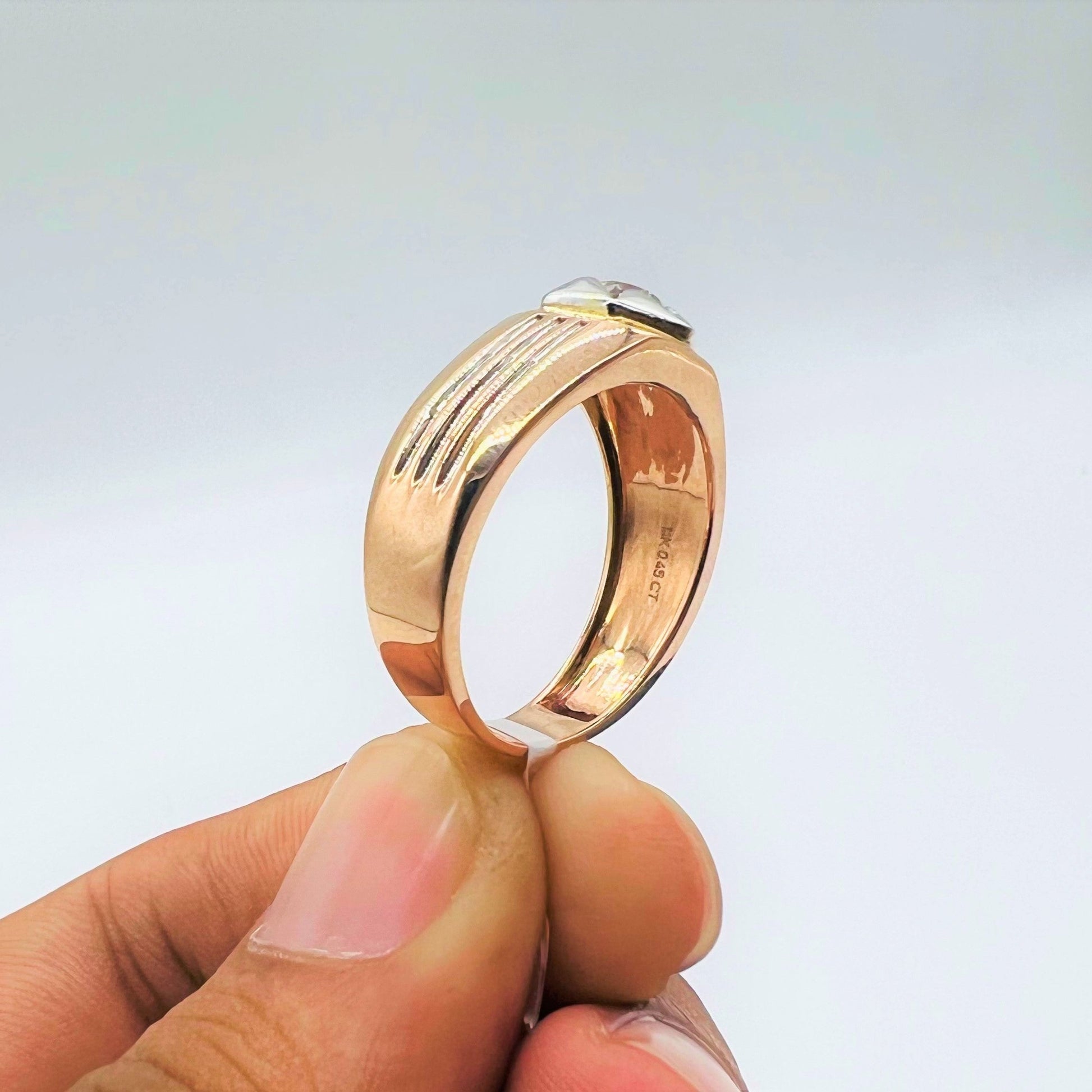 A man's hand displaying a gold solitaire diamond ring hold by his two fingers from the side.