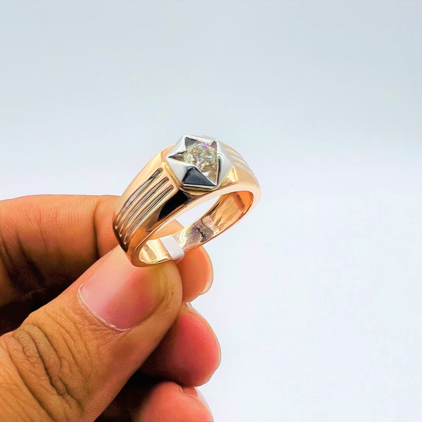 A man's hand displaying a gold solitaire diamond ring hold by his two fingers.