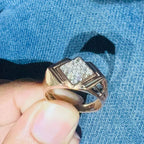 A man's hand holding a diamond ring with a rose gold band, featuring a solitaire diamond on top.