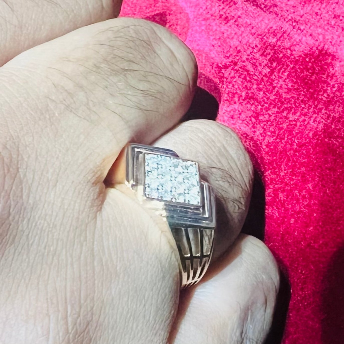 A man's hand holding a diamond ring with a rose gold band, featuring a solitaire diamond on top.