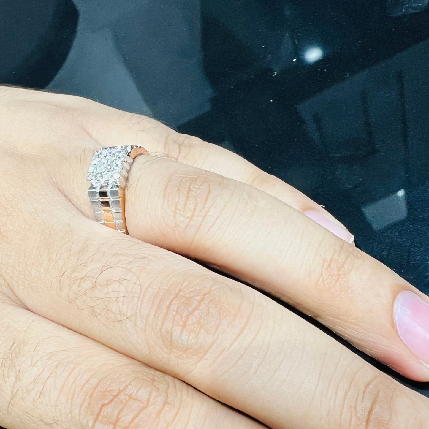 A man's hand displaying a gold diamond ring with a solid band and a small diamond inlay on the top surface.