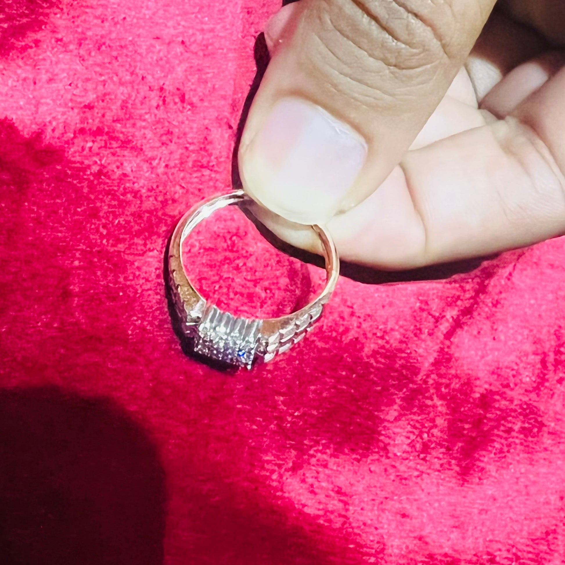 A man's hand displaying a gold diamond ring with a solid band and a small diamond inlay on the top surface.