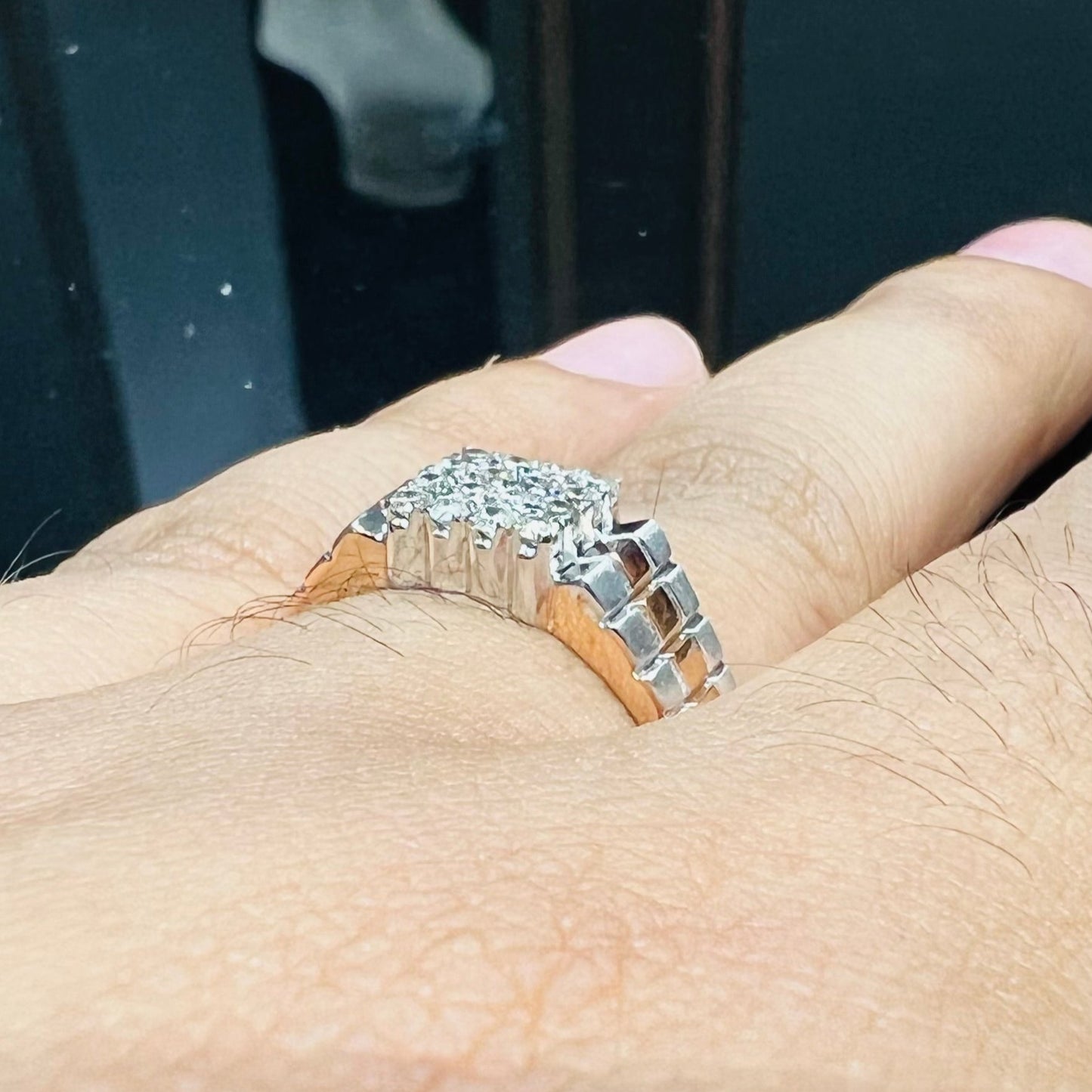 A man's hand displaying a gold diamond ring with a solid band and a small diamond inlay on the top surface.