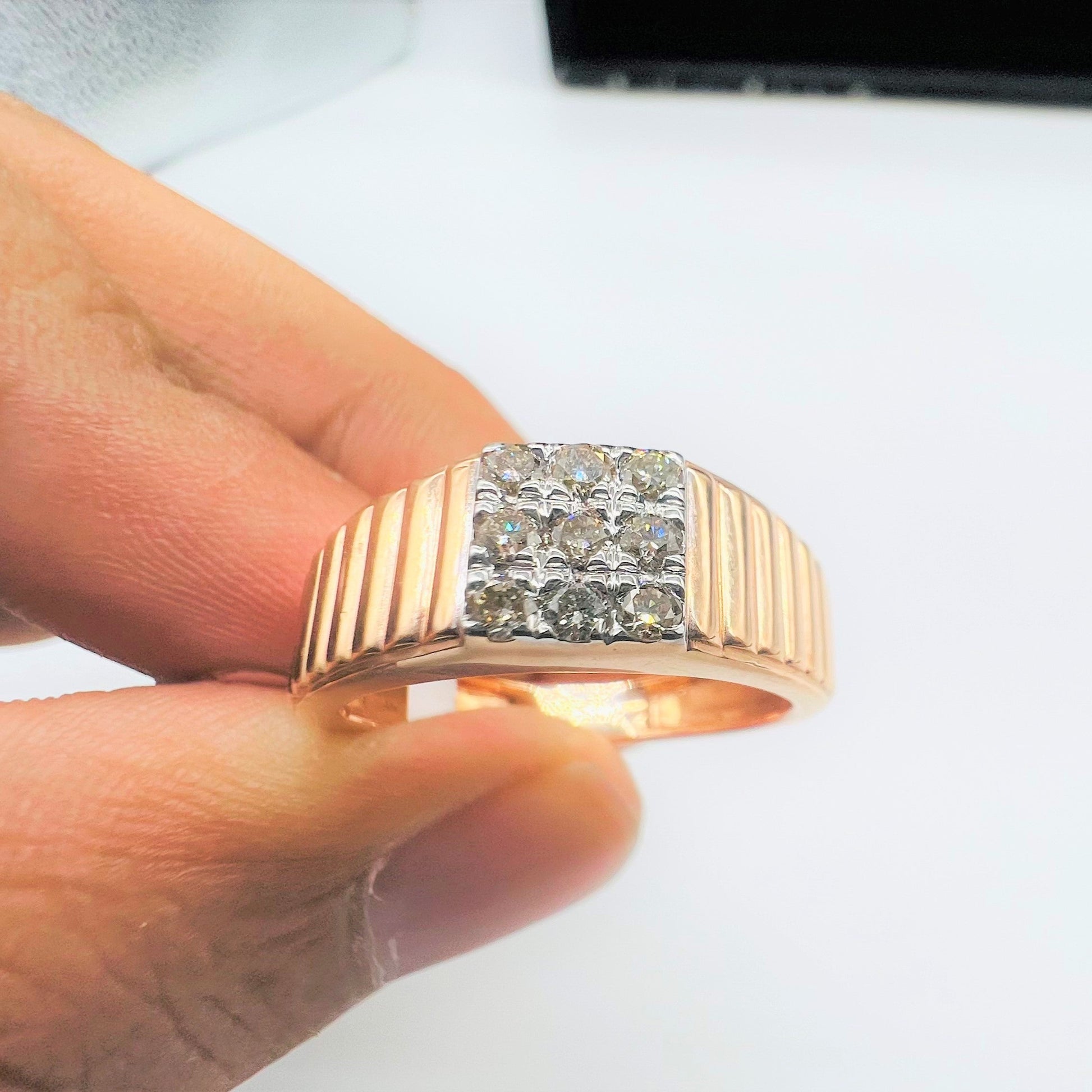 A man's hand holding a gold diamond ring with a solid gold band and a series of round cut diamonds set on top.
