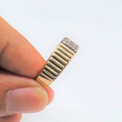 A man's hand holding a gold diamond ring with a solid gold band and a series of round cut diamonds set on top.