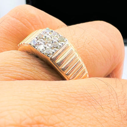 A man's hand holding a gold diamond ring with a solid gold band and a series of round cut diamonds set on top.