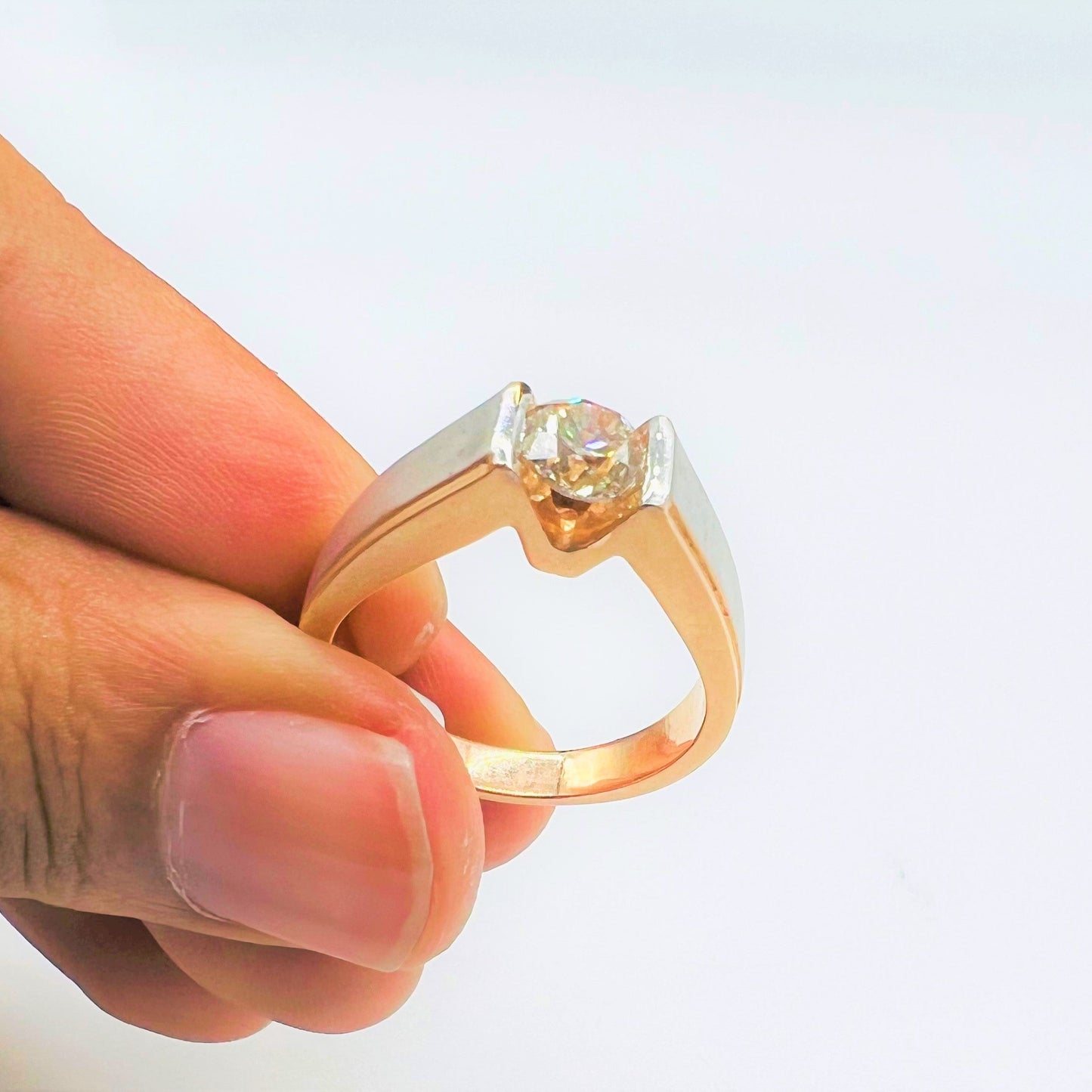 A man's hand holding a solitaire diamond ring with a gold band.