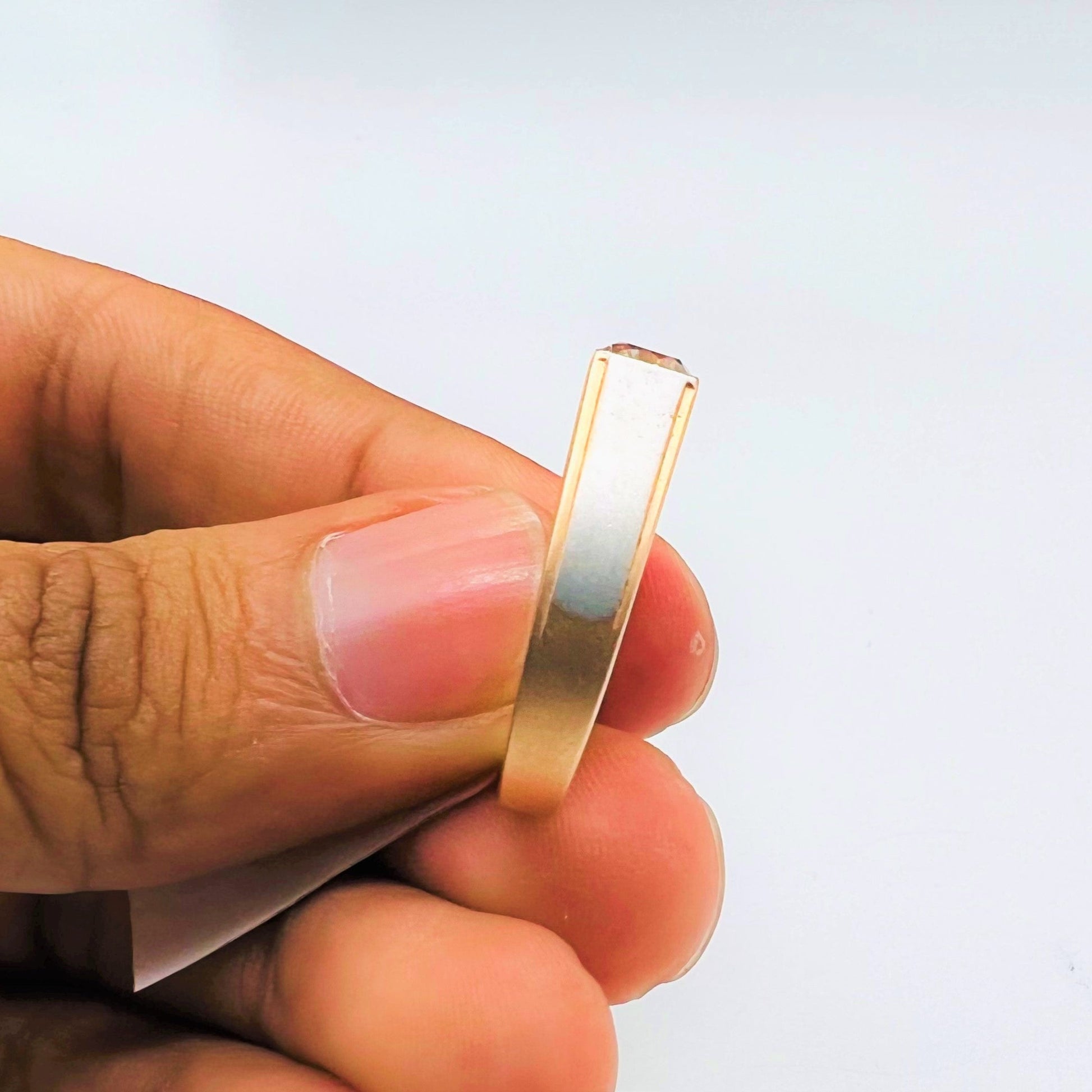 A man's hand holding a solitaire diamond ring with a gold band showing from vertical side.