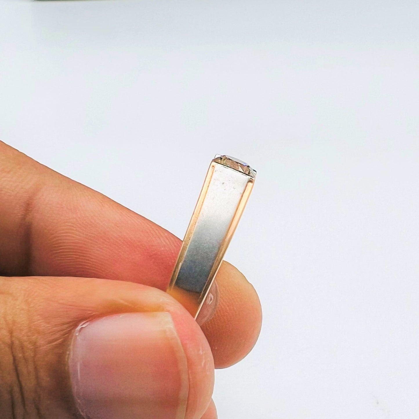 A man's hand holding a solitaire diamond ring with a gold band showing ring from vertical side.