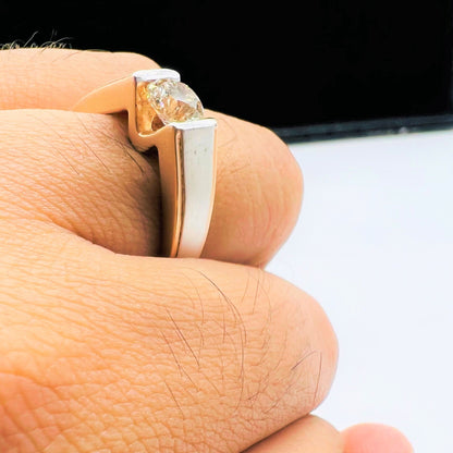 A man's hand holding a solitaire diamond ring with a gold band.