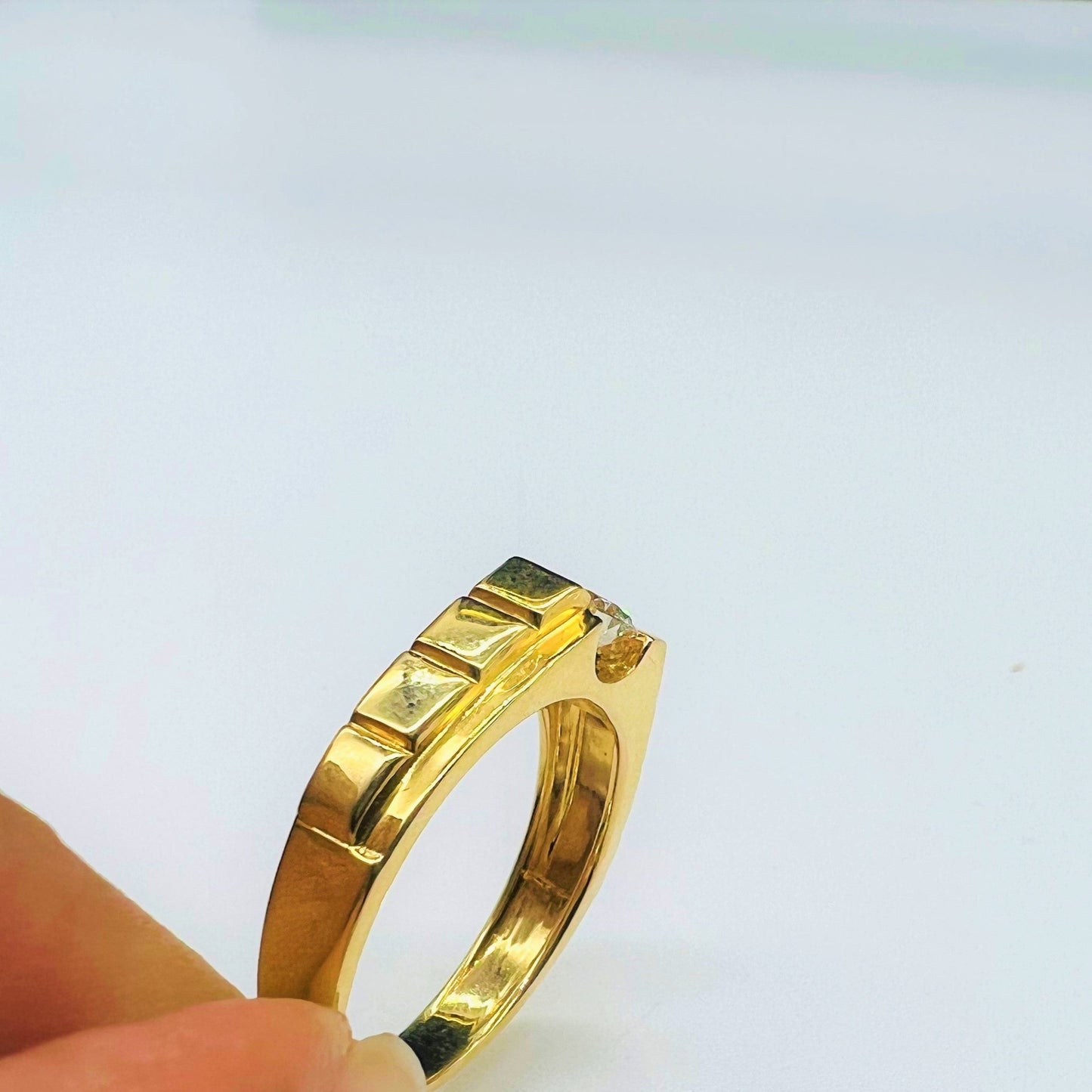 A gold band ring with a solitaire round-cut diamond set on top, held between fingers displayed from vertical side.