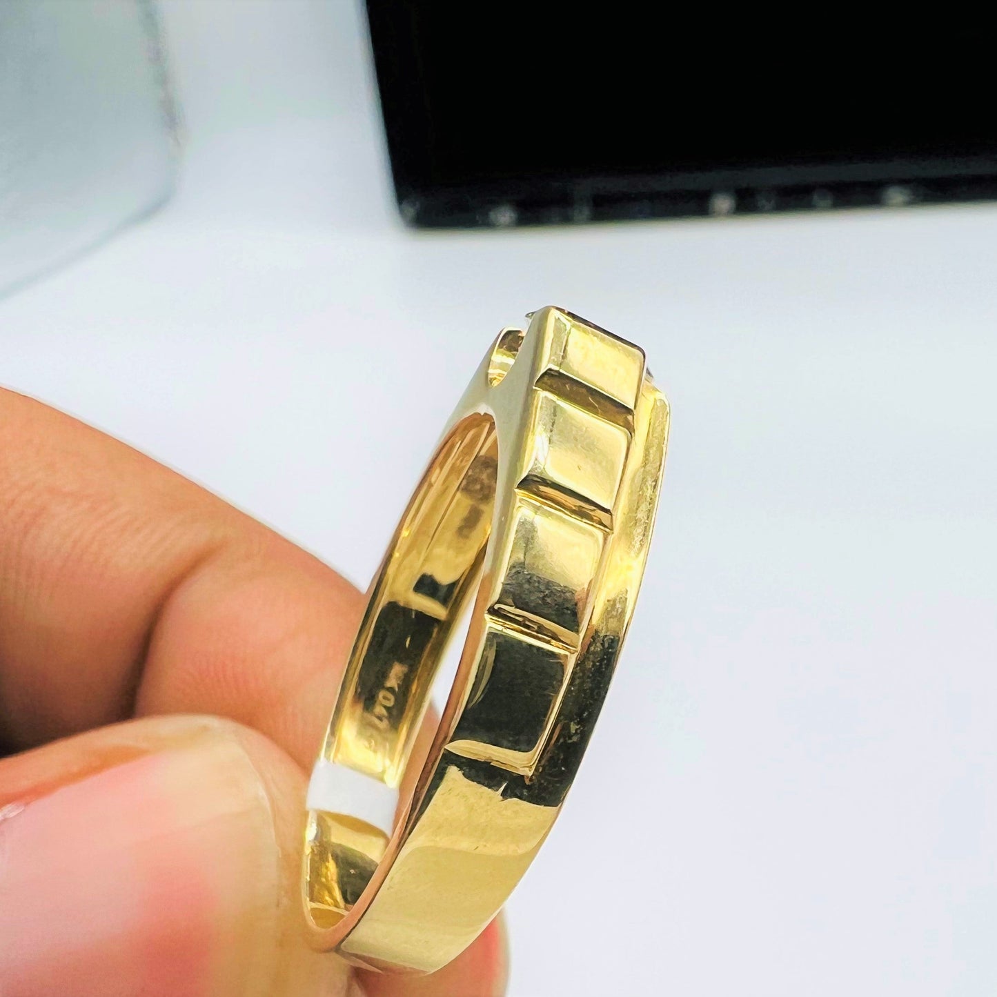 A gold band ring with a solitaire round-cut diamond set on top, held between fingers shown from vertical side.