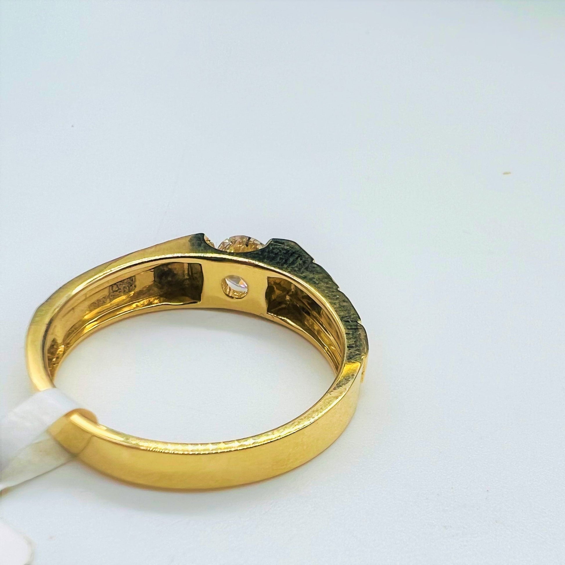 A gold band ring with a solitaire round-cut diamond set on top displayed on a white surface.