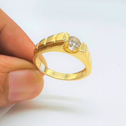 A gold band ring with a solitaire round-cut diamond set on top, held between fingers.