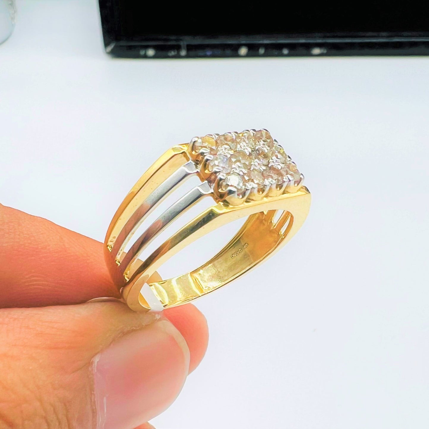 A man's hand holding a gold band ring with smaller round-cut diamonds with his two fingers.