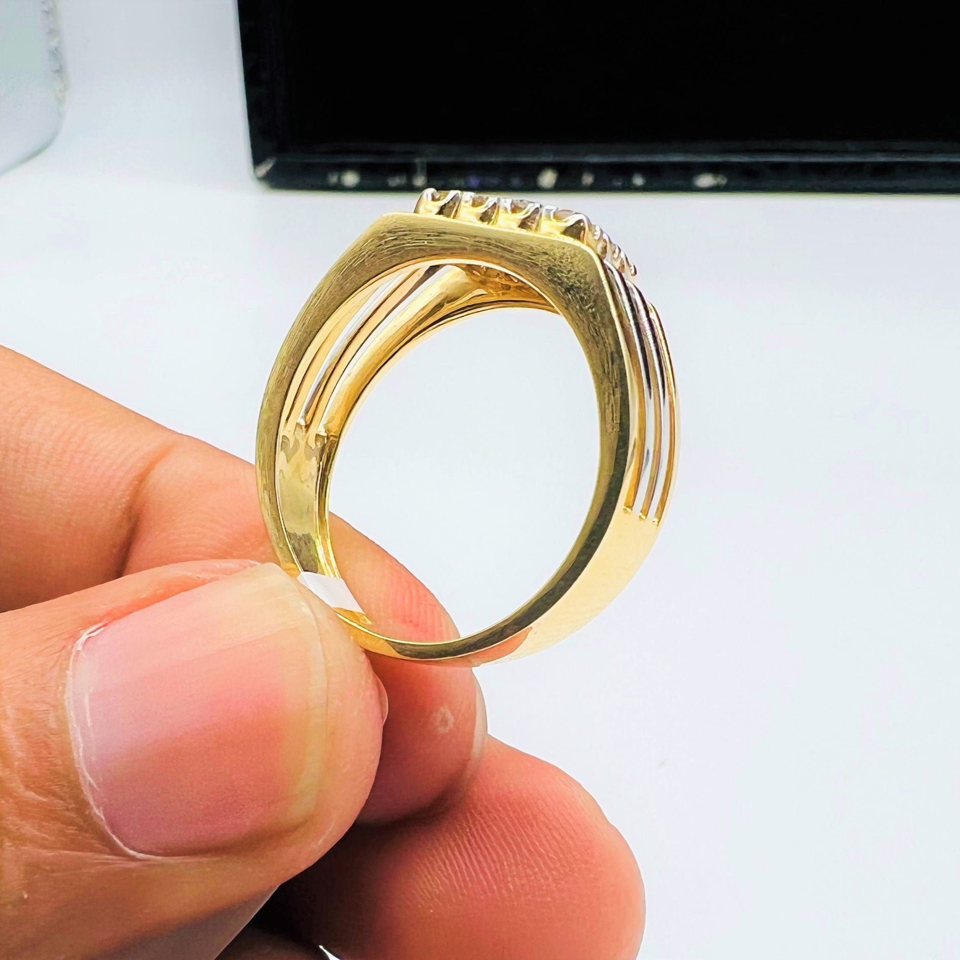 A man's hand holding a gold band ring with smaller round-cut diamonds.