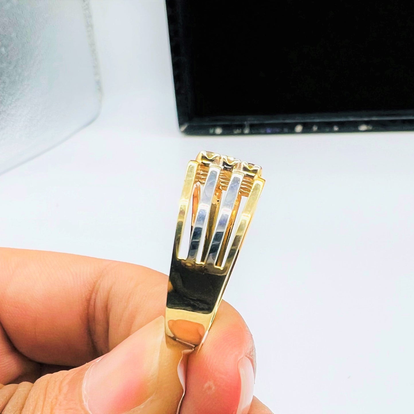 A man's hand displaying a gold band ring with smaller round-cut diamonds.