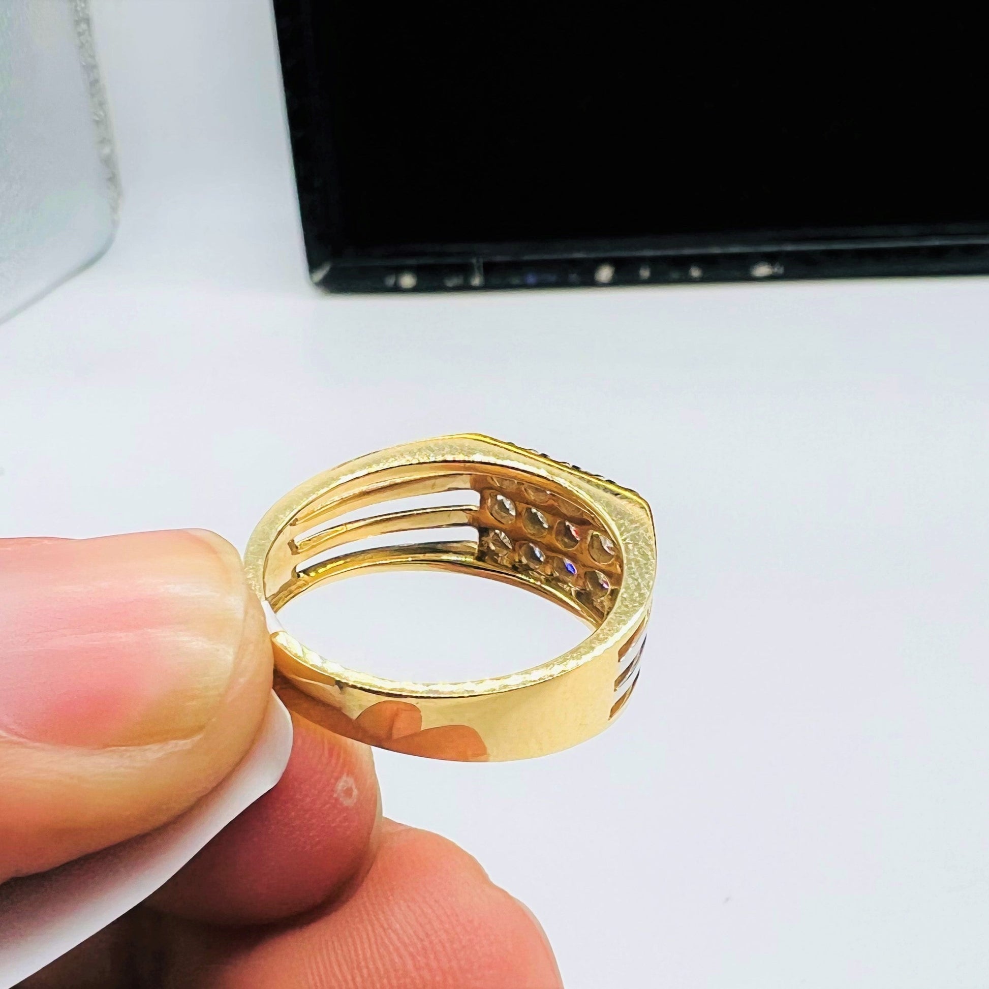 A man's hand displaying a gold band ring with smaller round-cut diamonds from back side.