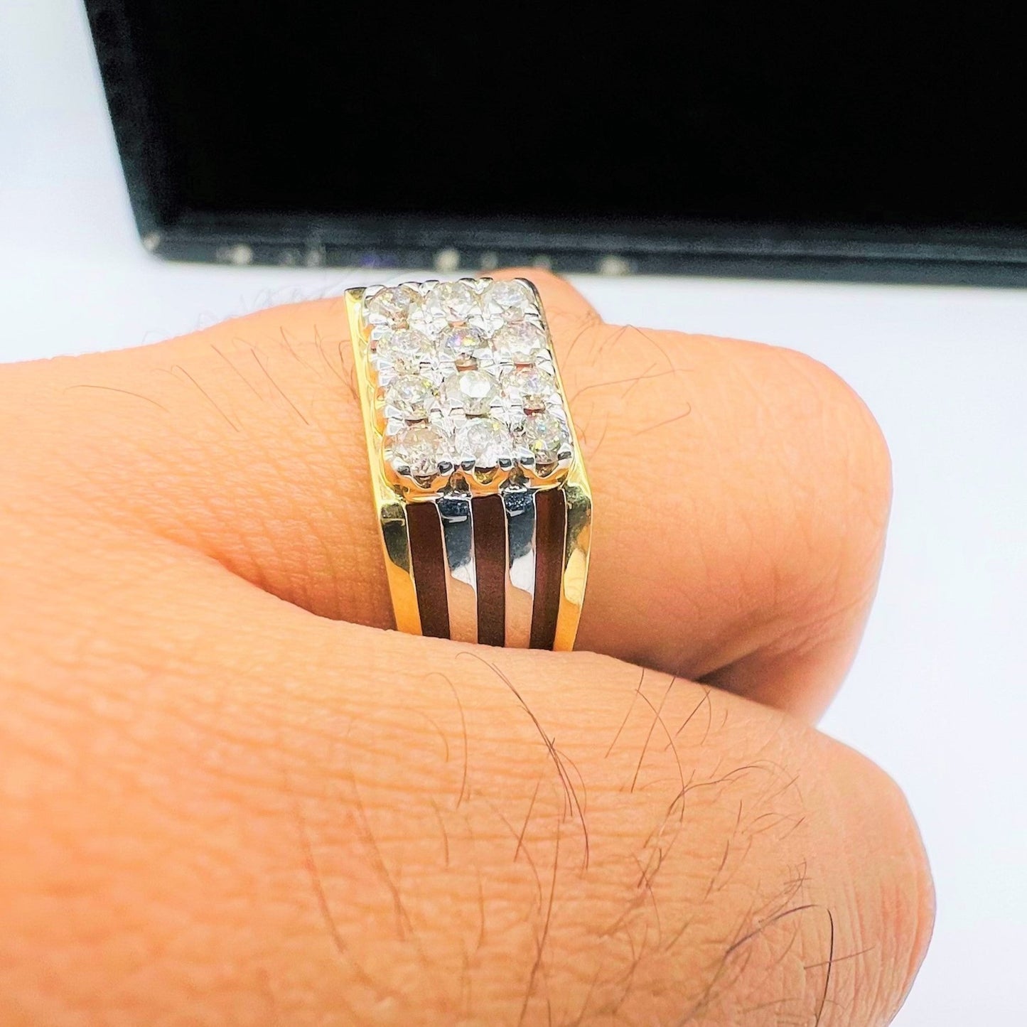A man's hand displaying a gold band ring with smaller round-cut diamonds.
