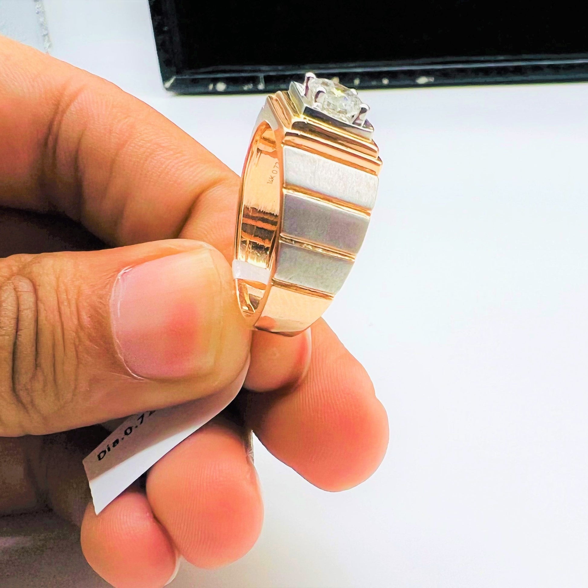 A man's hand holding a solitaire diamond ring with a gold band.