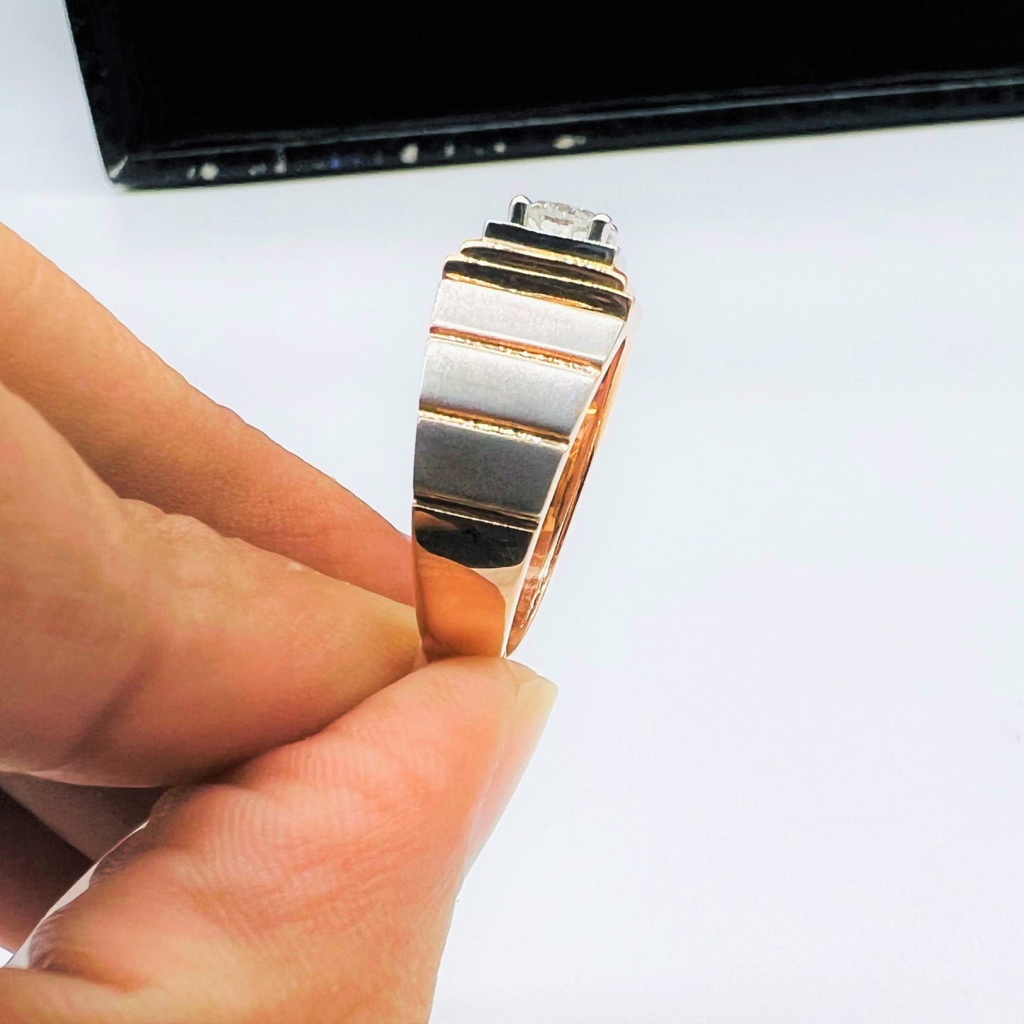 A man's hand showing a solitaire diamond ring with a gold band from vertical side.